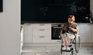 A woman using a wheelchair looks down as she makes coffee in an empty kitchen